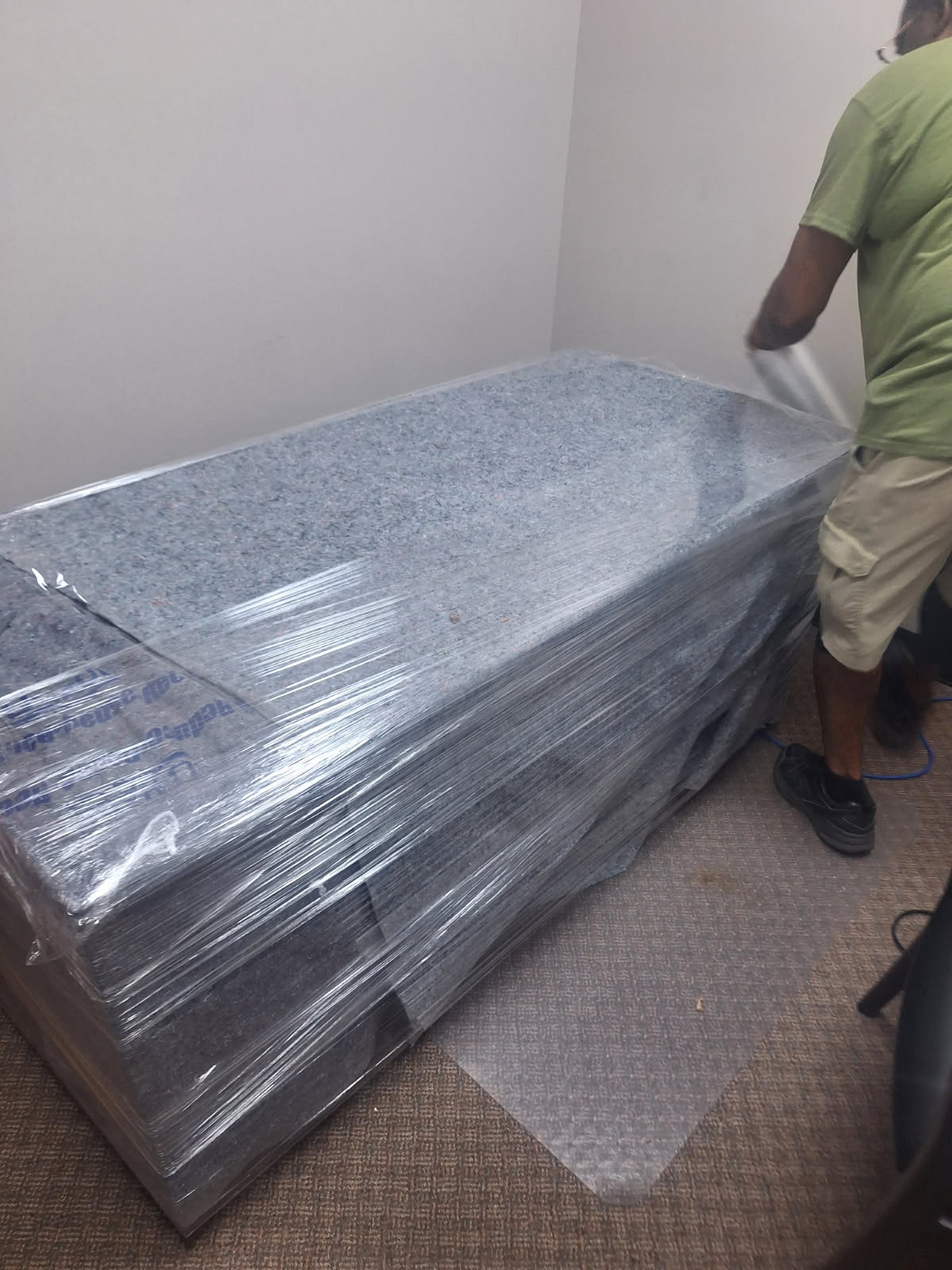 Wrapped casket displayed indoors with person in green shirt standing beside it