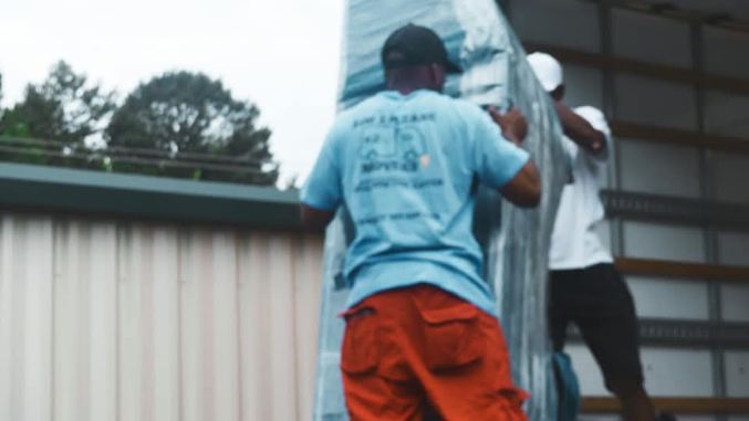 Two workers installing blue metal roofing panels on a residential structure