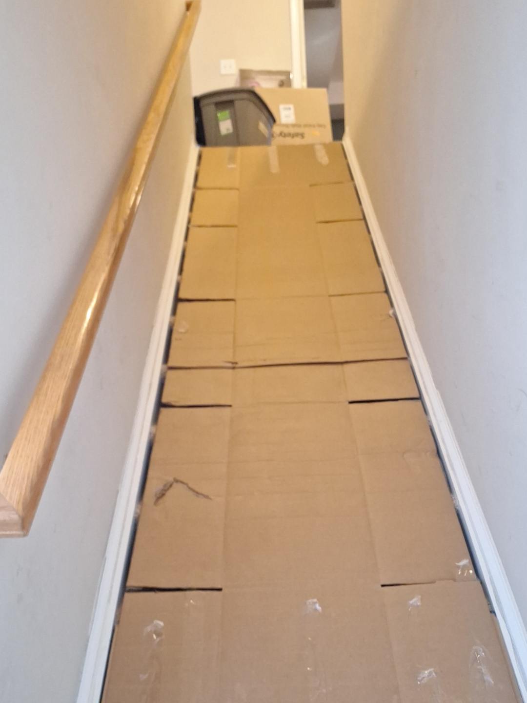 Narrow hallway with stacked cardboard boxes and wooden handrail along white wall