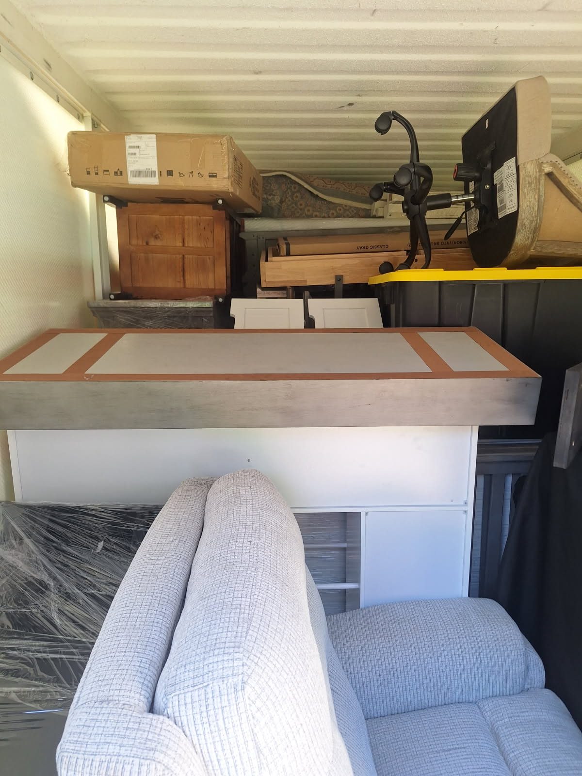 Interior of storage unit with couch, wooden furniture, cardboard box, and exercise bike