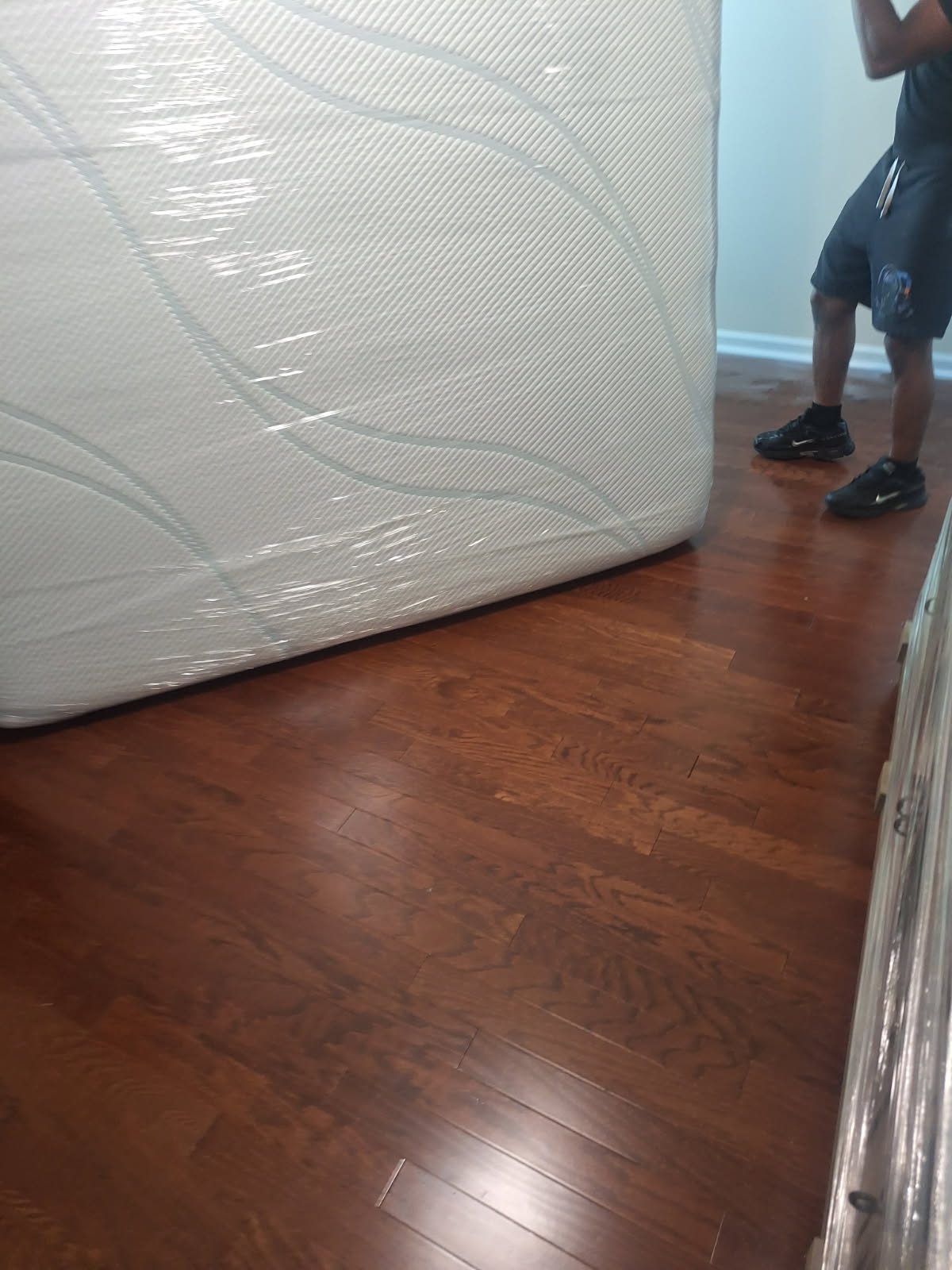 Wrapped mattress on wooden floor with person in Nike shoes standing nearby