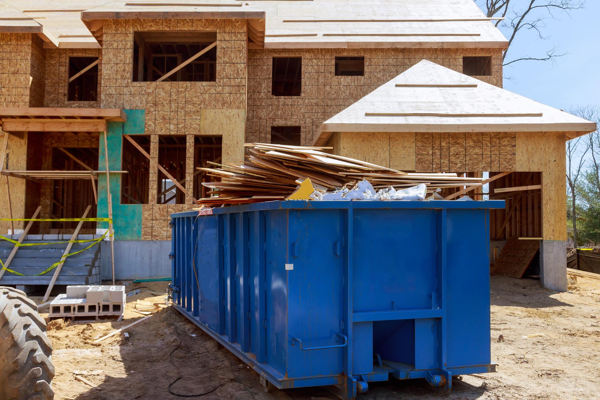 Construction site with brick framed house and blue waste dumpster