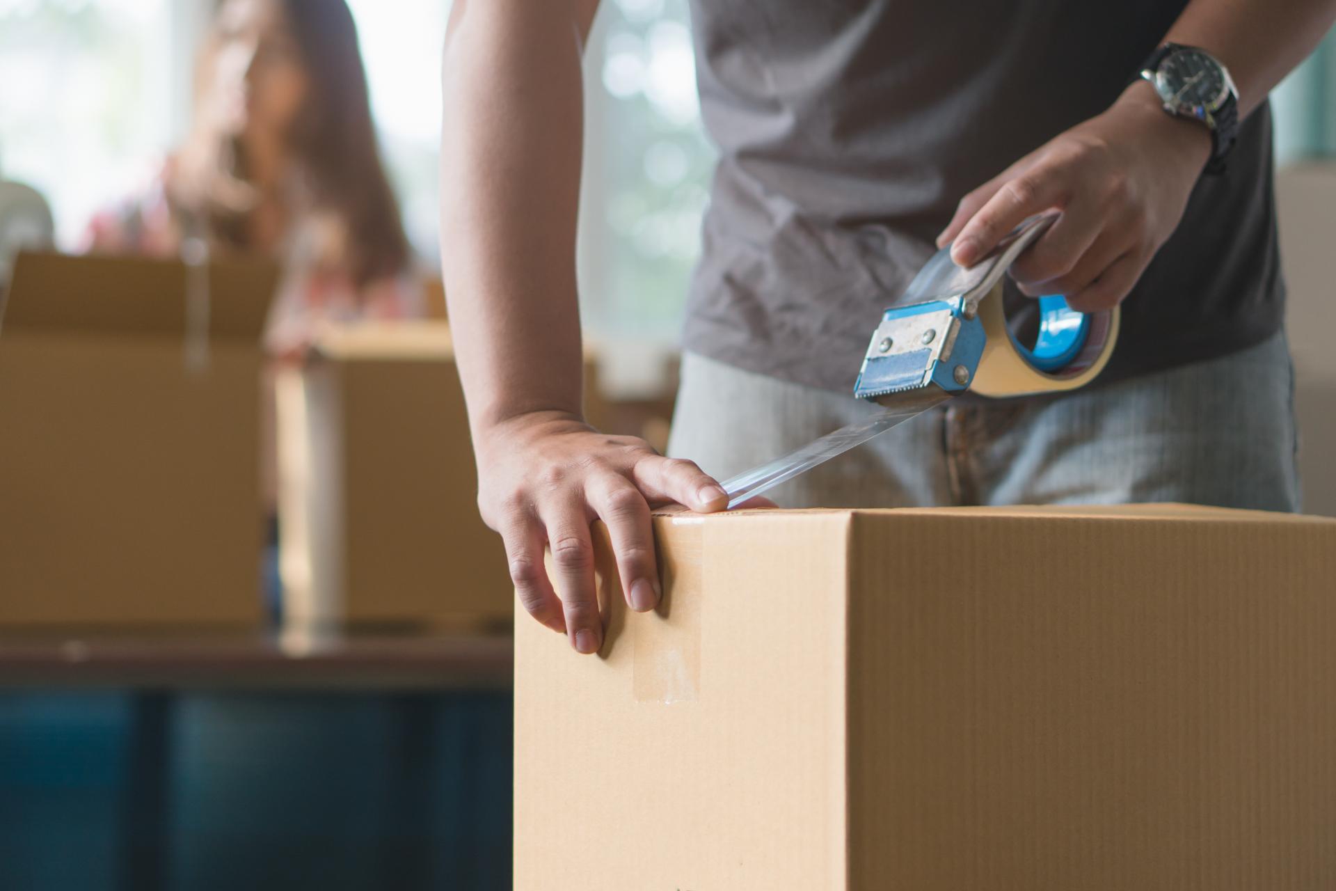 Worker sealing cardboard box with tape dispenser