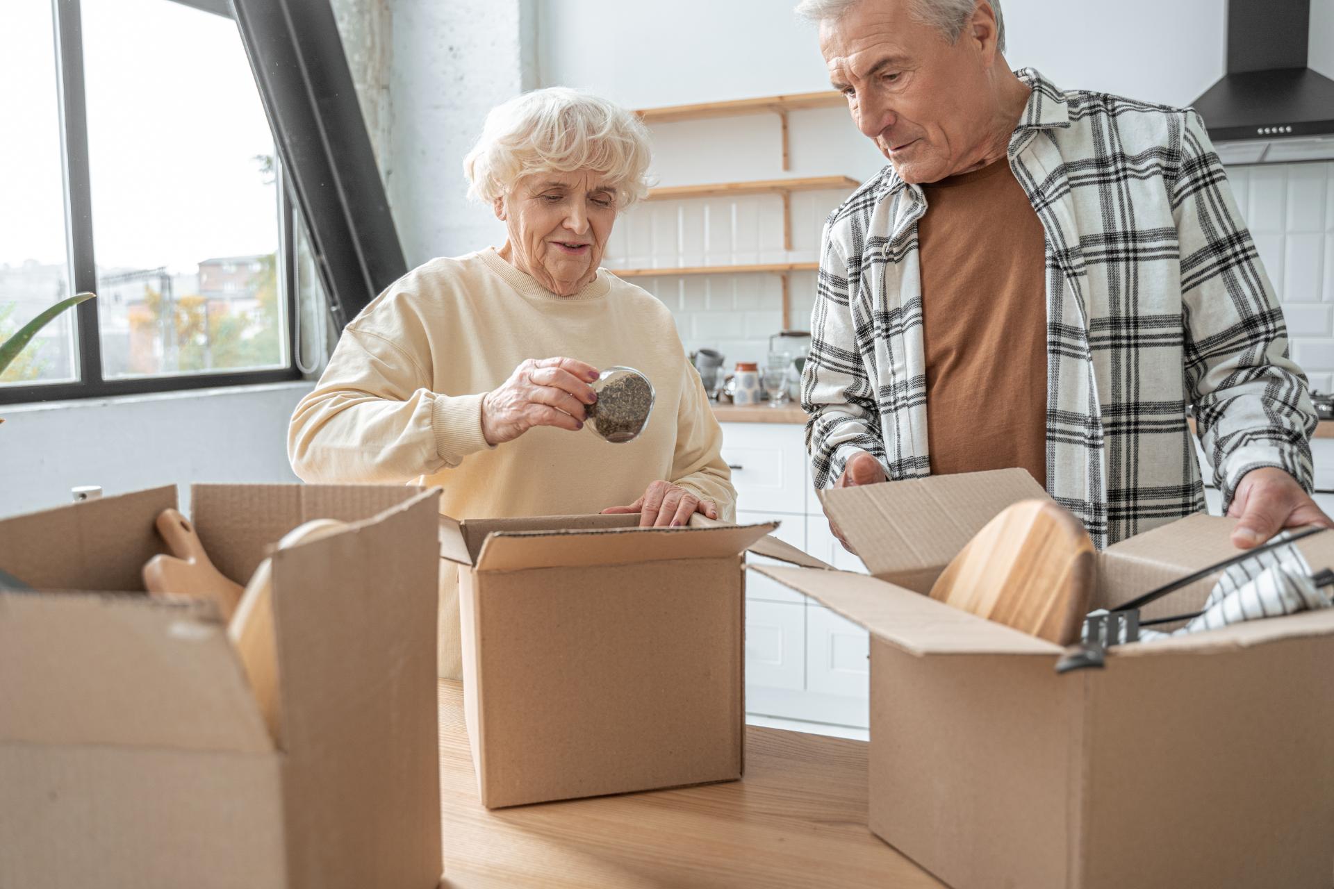 Senior couple unpacking cardboard boxes in modern kitchen during move